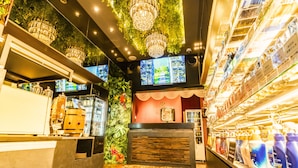 A modern bar area with a wooden counter, decorative plants, and a variety of bottled beverages. - Petit Bali Forest Shinjuku Sanchome (Tokyo)