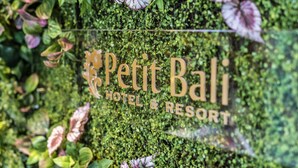 A sign for Petit Bali Hotel & Resort with a lush green background and some purple flowers. - Petit Bali Forest Shinjuku Sanchome (Tokyo)