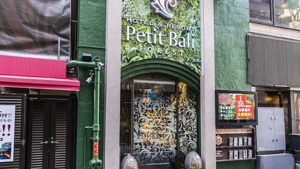 The exterior of Hotel & Resort Petit Bali Forest with a green facade, decorative entrance, and two large vases in front. - Petit Bali Forest Shinjuku Sanchome (Tokyo)