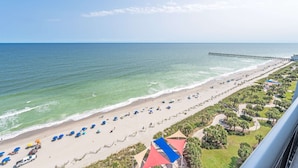 A beach with umbrellas, a pier, and a view of the ocean. - Amaze 18th floor Direct Ocean front Views & Pools (Myrtle Beach)
