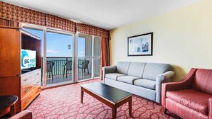 A hotel room with a sofa, a red armchair, a coffee table, and a sliding glass door leading to a balcony with outdoor furniture. - Amaze 18th floor Direct Ocean front Views & Pools (Myrtle Beach)