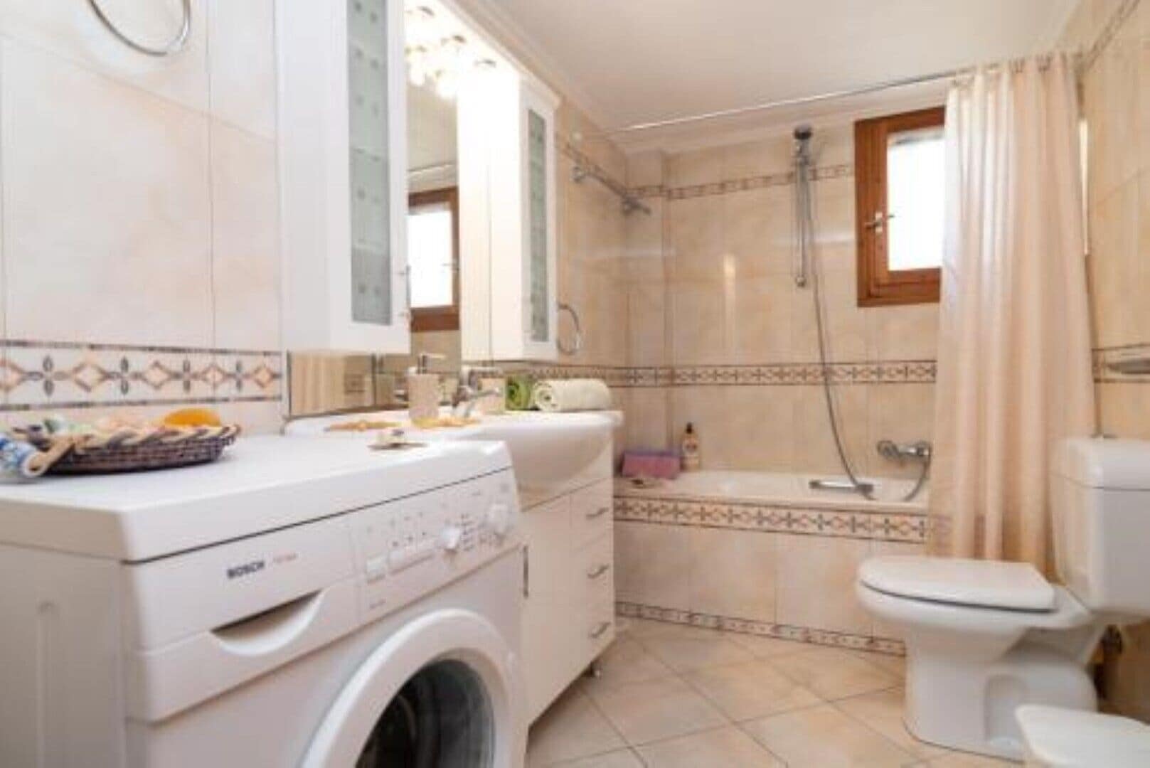 A compact bathroom with a washing machine, toilet, and shower.