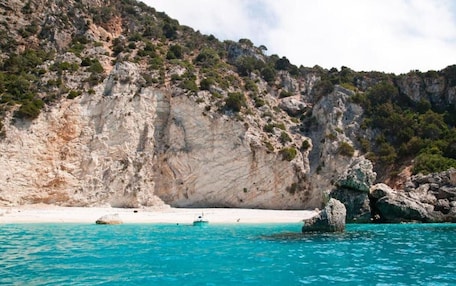 A coastal landscape with a rocky cliff, clear turquoise waters, and a boat anchored near the shore.
