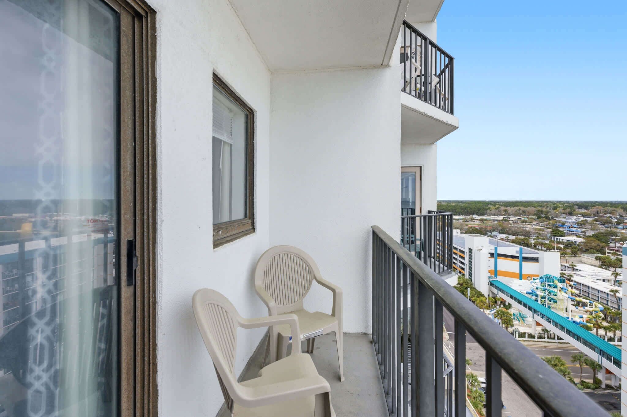 Een balkon met twee stoelen, een raam en uitzicht op een stadsbeeld.
