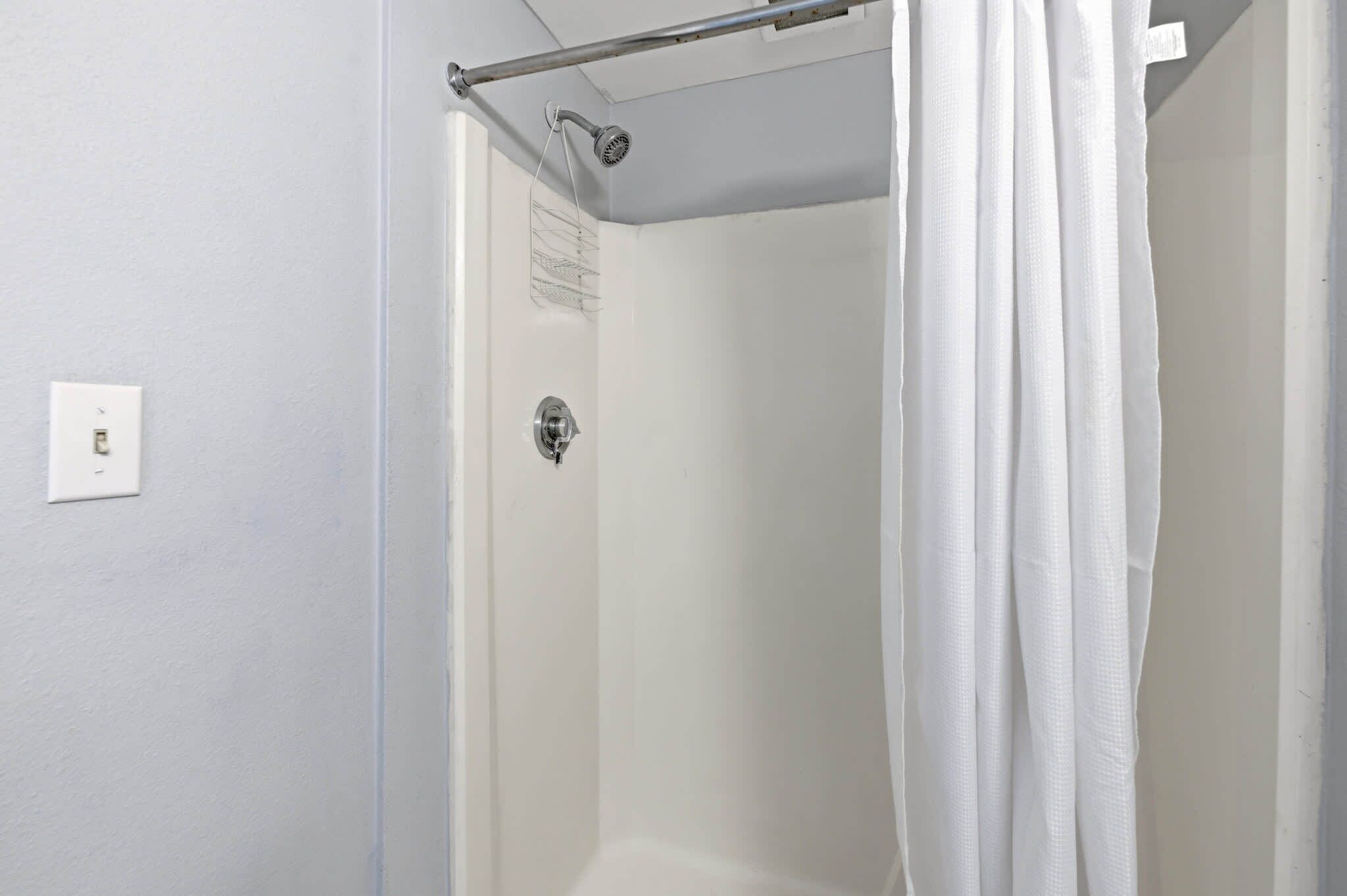 Eine Dusche mit einer Metallstange und einem weißen Duschvorhang.