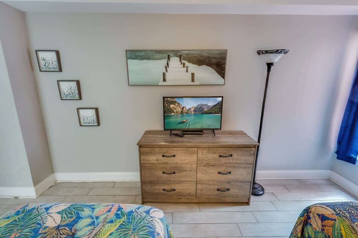 Quarto com cômoda de madeira, televisão de tela plana e pintura de uma escada que deságua em um corpo d'água.