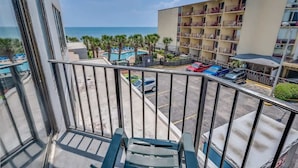 A balcony with a view of a hotel building, a swimming pool, and parked cars. - Palace Resort 2BR, Pools & Ocean Views, 2nd Floor (Myrtle Beach)