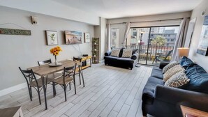 A modern living room with a dining table, black leather sofa, and a balcony with a view of the city. - Palace Resort 2BR, Pools & Ocean Views, 2nd Floor (Myrtle Beach)