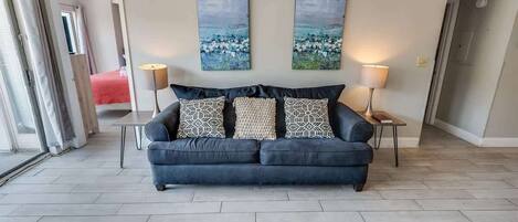 A modern living room with a dark blue sofa, two patterned throw pillows, and two abstract landscape paintings on the wall.
