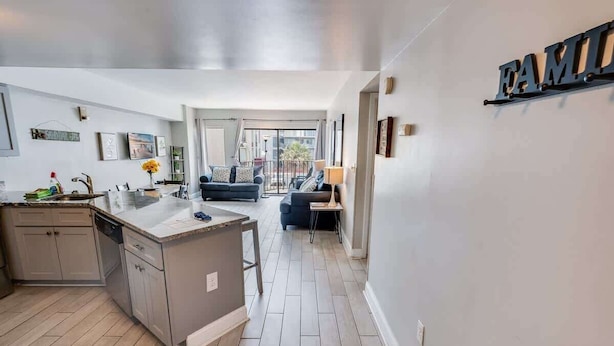 A modern kitchen with a central island, a dining area with a sofa, and a balcony with a view. - Palace Resort 2BR, Pools & Ocean Views, 2nd Floor (Myrtle Beach)