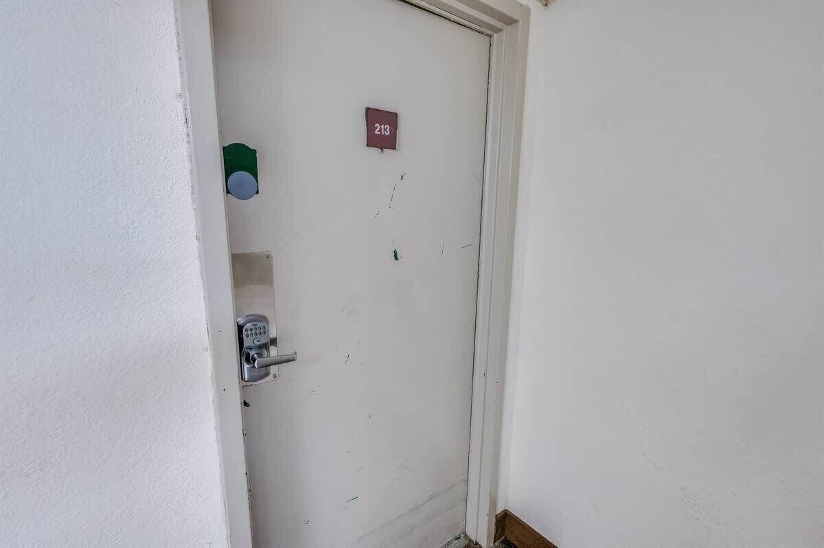 A white door with a numeric keypad lock, a small sign with the number 213, and a green object on the wall to the left.