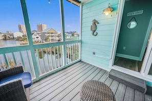 Een turquoise terras met rieten meubels, een seahorse decoratie, en een bordje 'Beach House'.