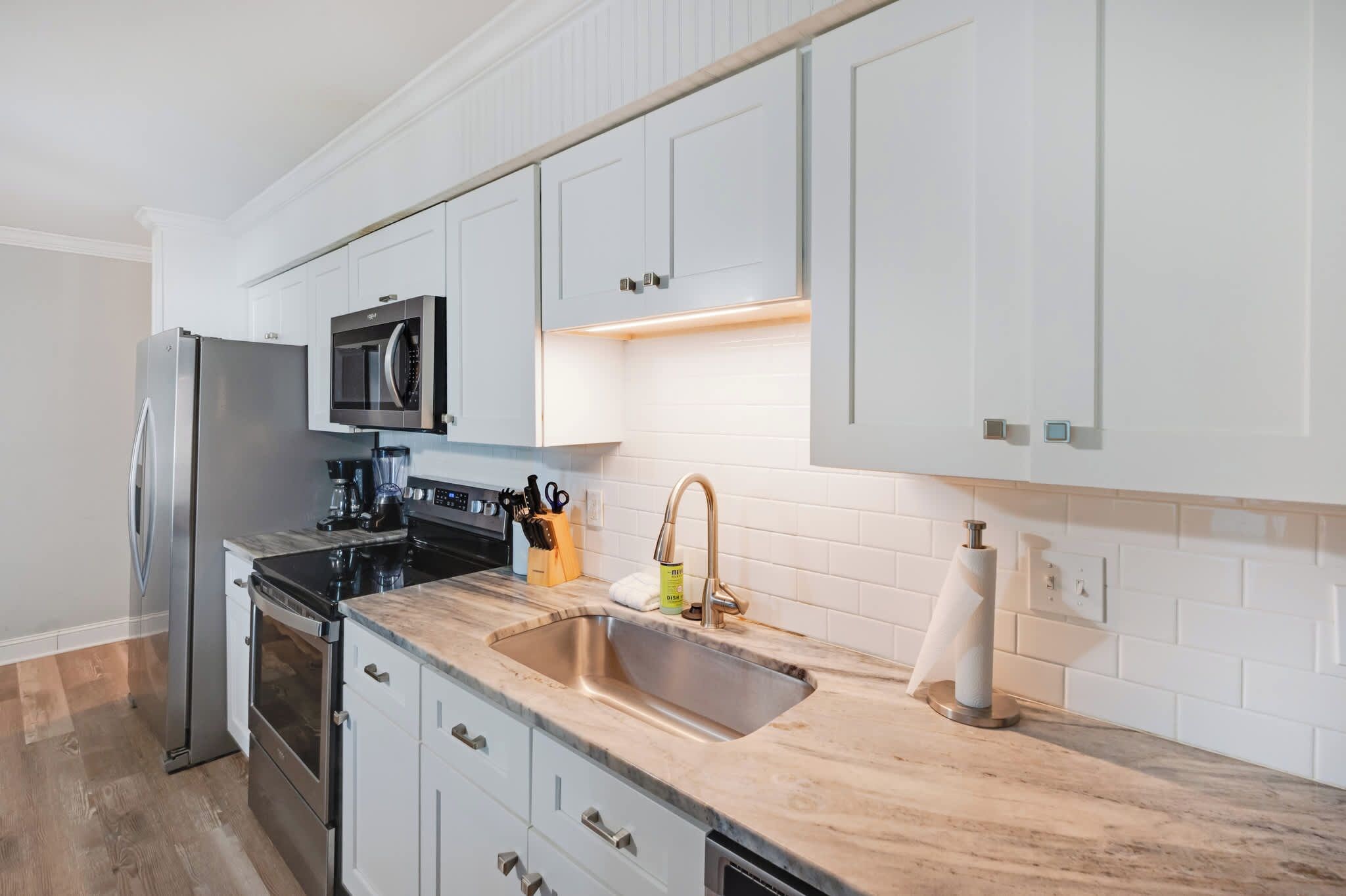 A modern kitchen with white cabinetry, stainless steel appliances, and a marble countertop.