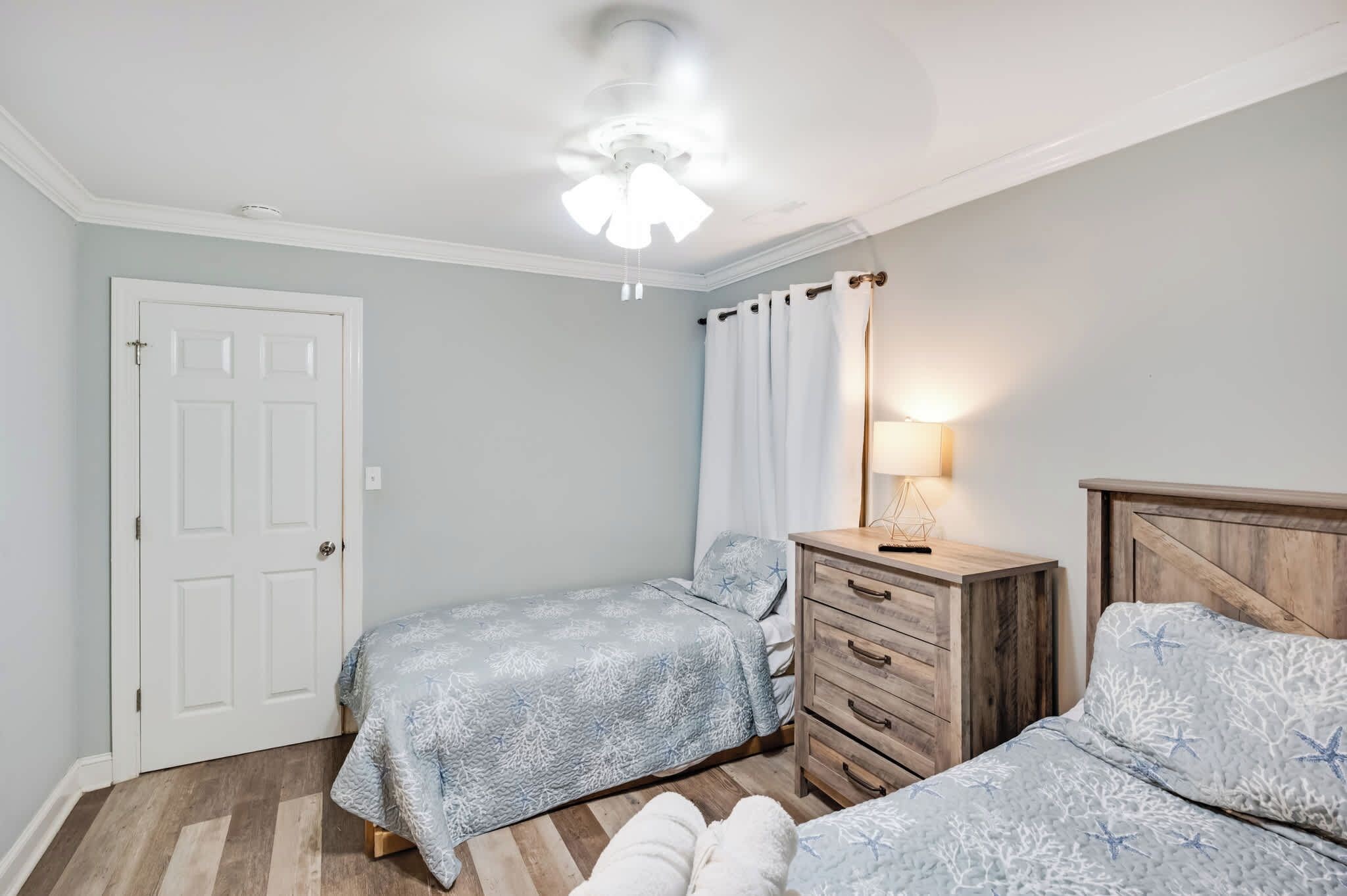 A bedroom with two beds, a wooden dresser, a ceiling fan, and a door.