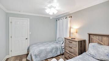 A bedroom with two beds, a wooden dresser, a ceiling fan, and a door.