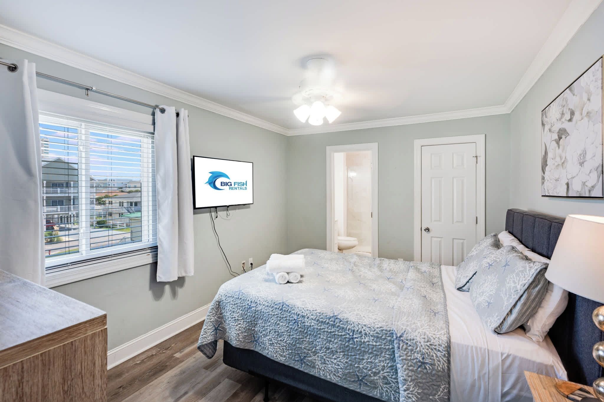 A bedroom with a bed, a TV, a window with curtains, and a door.