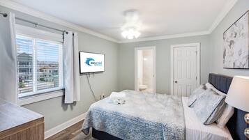 A bedroom with a bed, a TV, a window with curtains, and a door.