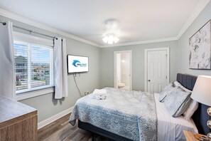 A bedroom with a bed, a TV, a window with curtains, and a door.