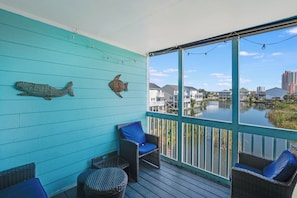 A covered outdoor area with a view of a body of water, featuring wicker furniture and decorative fish wall art.