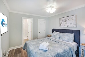 Ein Schlafzimmer mit Bett, Deckenventilator, gerahmtem Kunstwerk und einer Tür.