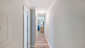 A hallway with a wooden floor, a door on the left, and a blue chair in the distance.