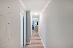 A hallway with a wooden floor, a door on the left, and a blue chair in the distance.