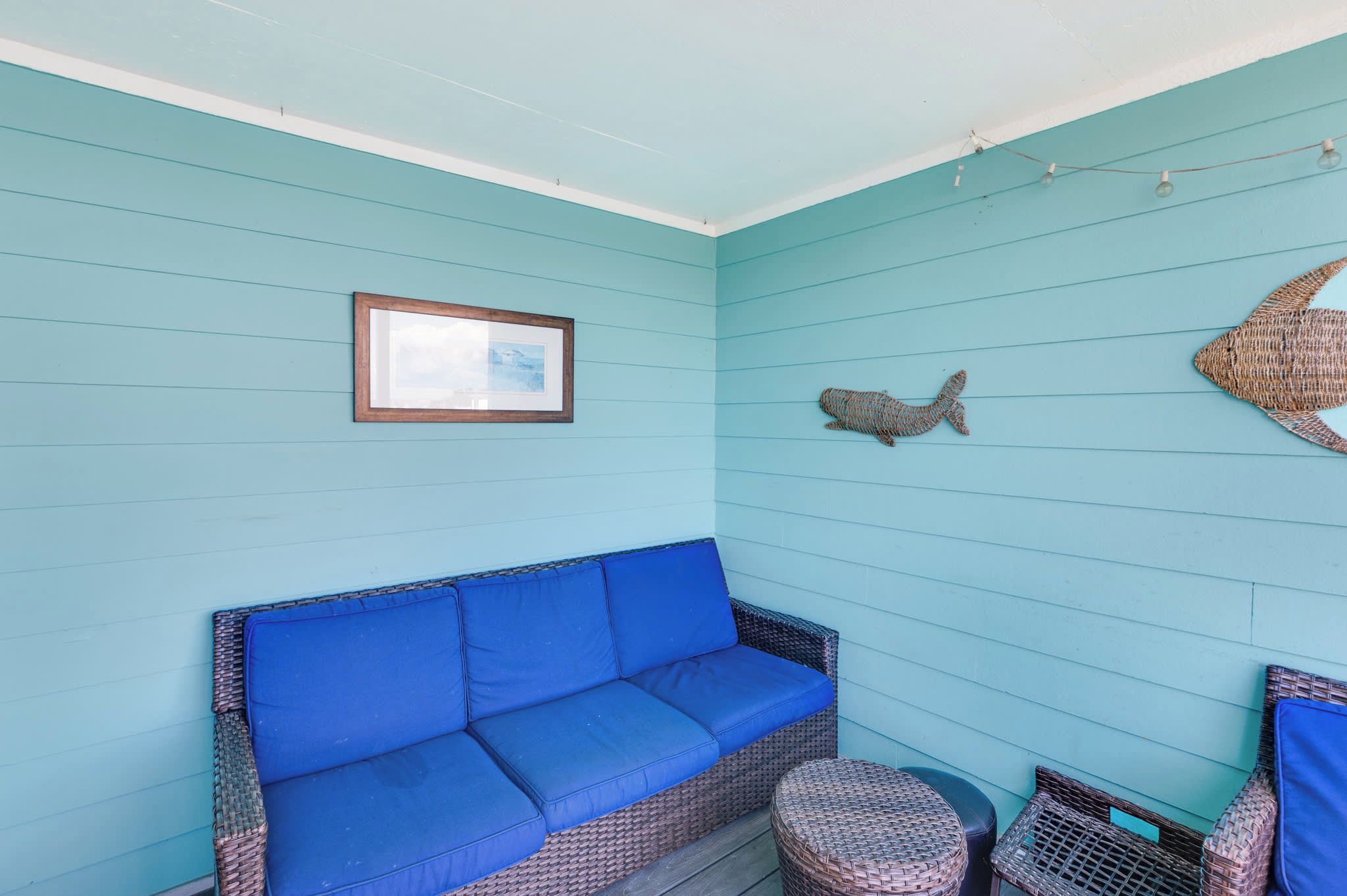 A room with a blue sofa, wicker furniture, a framed picture, and a decorative fish wall hanging.