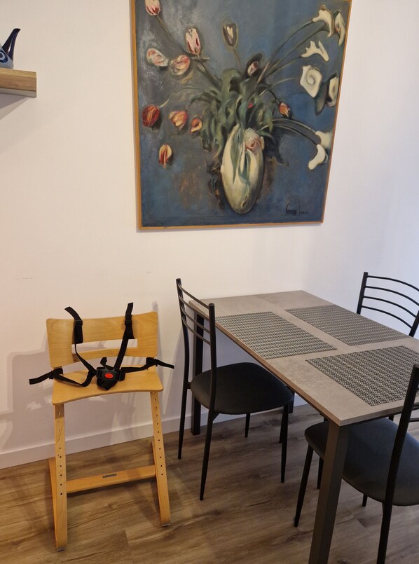 Un coin repas avec un banc en bois, une table entourée de chaises noires et un tableau représentant des fleurs accroché au mur.