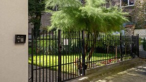 A gated entrance with a metal fence, a small tree, and a building in the background.