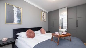 A modern bedroom with a bed, bedside tables, a bedside lamp, a mirror, and a wardrobe.