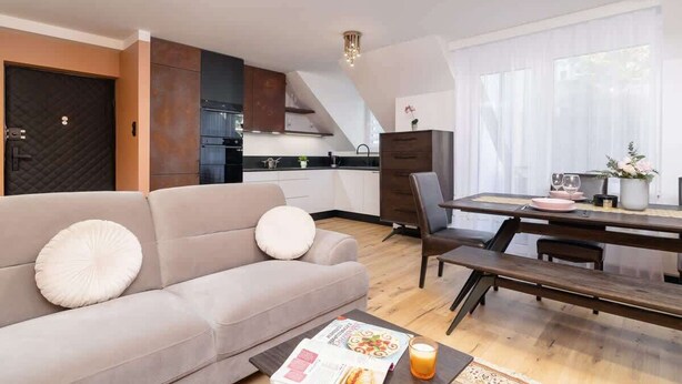 A modern living room with a sofa, a dining table with chairs, and a kitchen in the background.