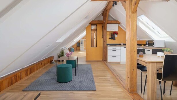 A modern loft apartment with a sloped ceiling, wooden beams, a kitchen area, and a dining space. - Air-conditioned apartment in Kazimierz | Parking | Workplace (Kraków)