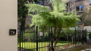A gated entrance with a metal fence, a small tree, and a building in the background. - Air-conditioned apartment in Kazimierz | Parking | Workplace (Kraków)