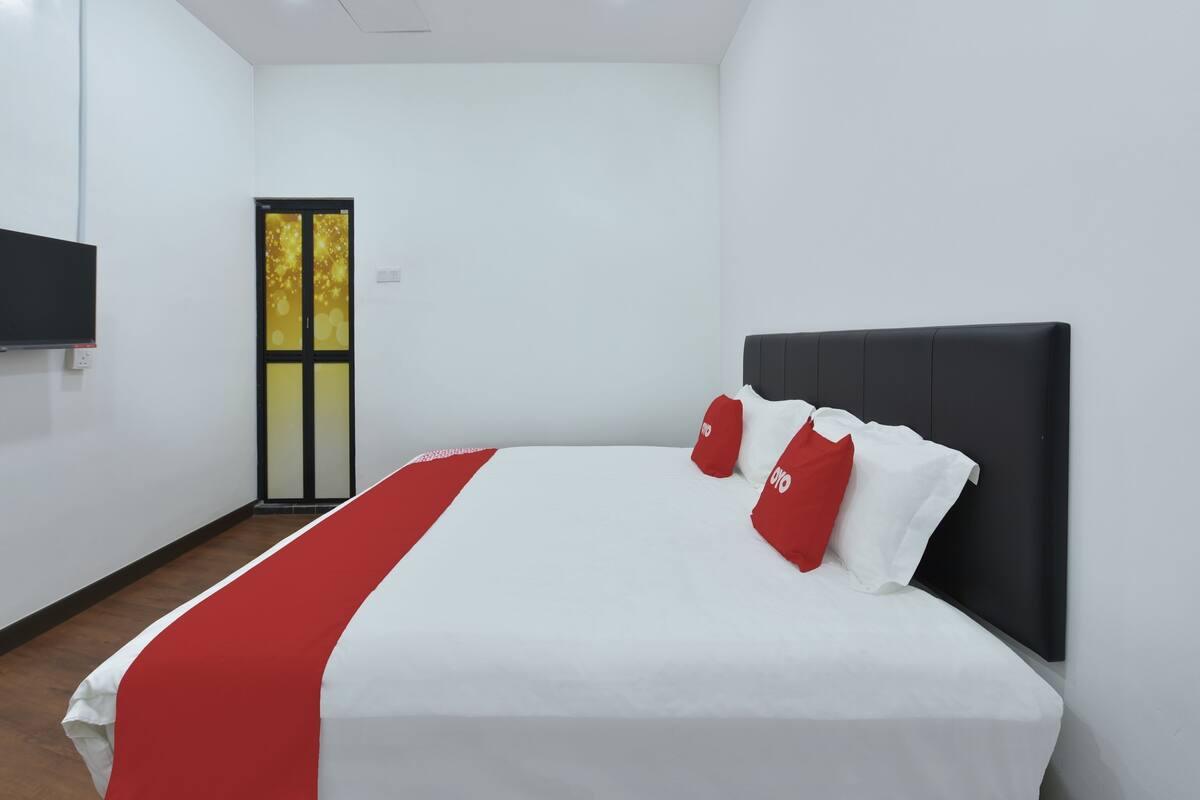 Habitación de hotel con una cama grande, un televisor de pantalla plana en la pared y una puerta con panel de vidrio.