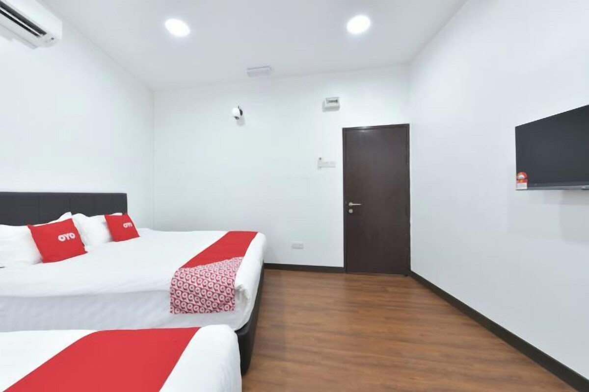A hotel room with two beds, a dark door, a mounted TV, and an air conditioning unit.