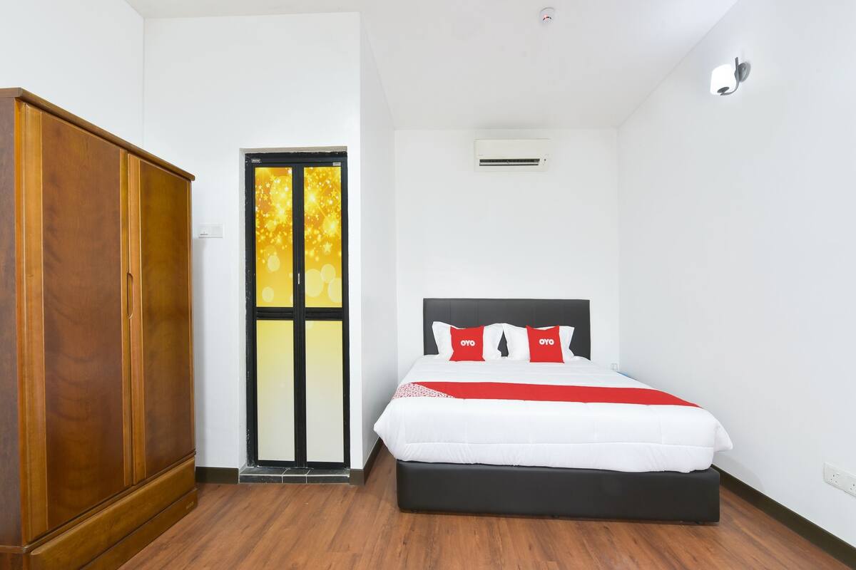 Un dormitorio con un armario de madera, una cama con ropa de cama blanca y almohadas rojas, y una puerta con detalles dorados.