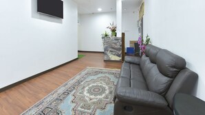 Un intérieur moderne avec un canapé en cuir gris, un tapis à motifs, un téléviseur à écran plat fixé au mur et un comptoir d’accueil agrémenté de plantes.