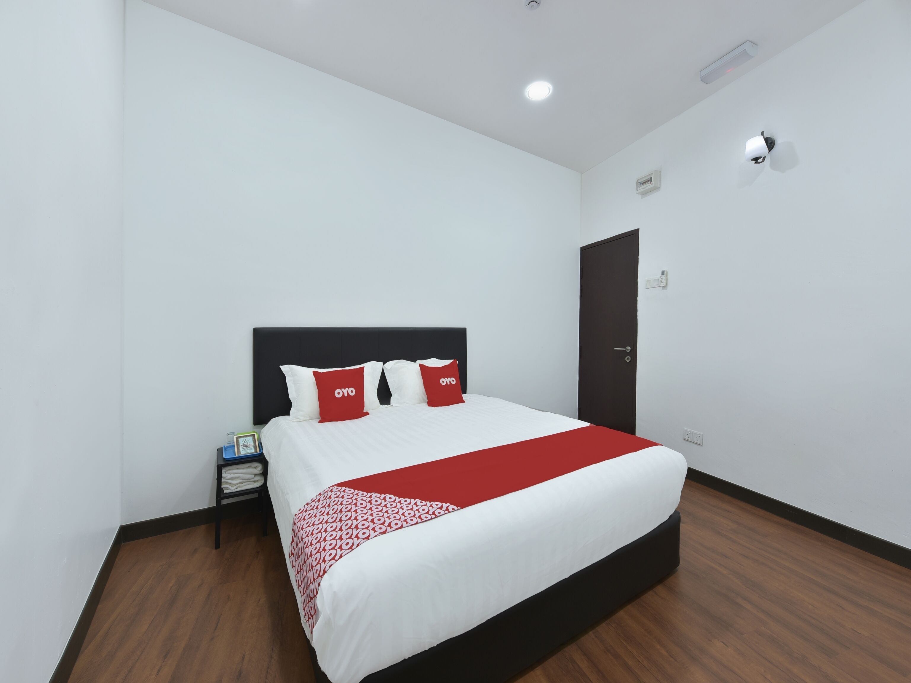A neatly arranged hotel room with a bed, a nightstand, a door, and a wall-mounted light fixture.