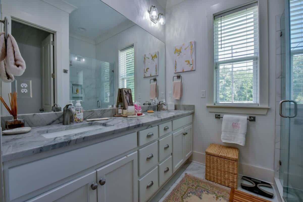 A modern bathroom with a large mirror, two sinks, a shower, and a small wicker basket.