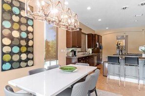 A modern kitchen with a dining area, featuring a white table, grey chairs, and a unique light fixture.