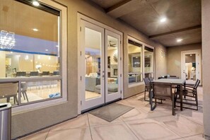 A covered patio area with a dining table and chairs, a sliding glass door leading to an indoor space, and a ceiling fan.