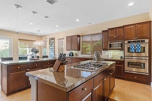 A spacious kitchen with dark wood cabinets, a central island with a stove, and a large window providing natural light.