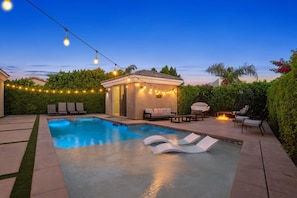 A swimming pool with lounge chairs, a small gazebo with string lights, and a fire pit area.