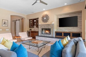A modern living room with a fireplace, a flat-screen TV, and a ceiling fan.