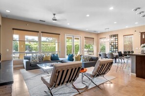A spacious living area with a sofa, chairs, a dining table, and a kitchen area with a bar.