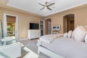 A bedroom with a bed, a television, a dresser, and a ceiling fan.