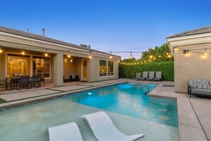 Una piscina con sillas de descanso, un patio con mobiliario exterior y luces colgantes.