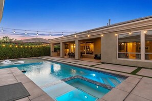 A swimming pool with a hot tub, outdoor seating, and string lights.