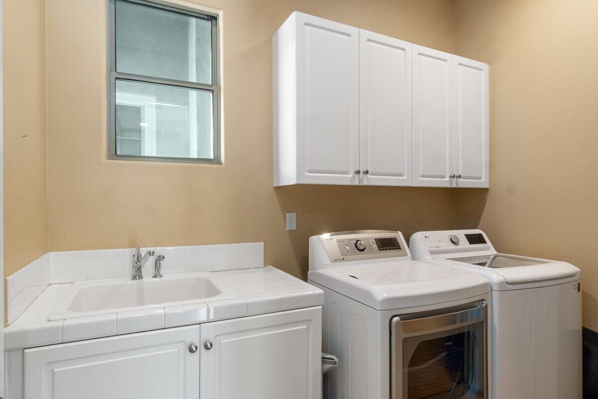 A laundry room with a sink, two washing machines, and a cabinet above the machines.