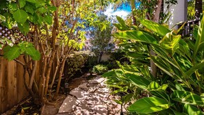 A garden pathway with stone slabs, surrounded by lush green foliage and a wooden fence. - North Park Haven Summ (San Diego)